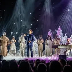Ein Sänger inklusive Chor auf einer Bühne in weihnachtlichem Setting.