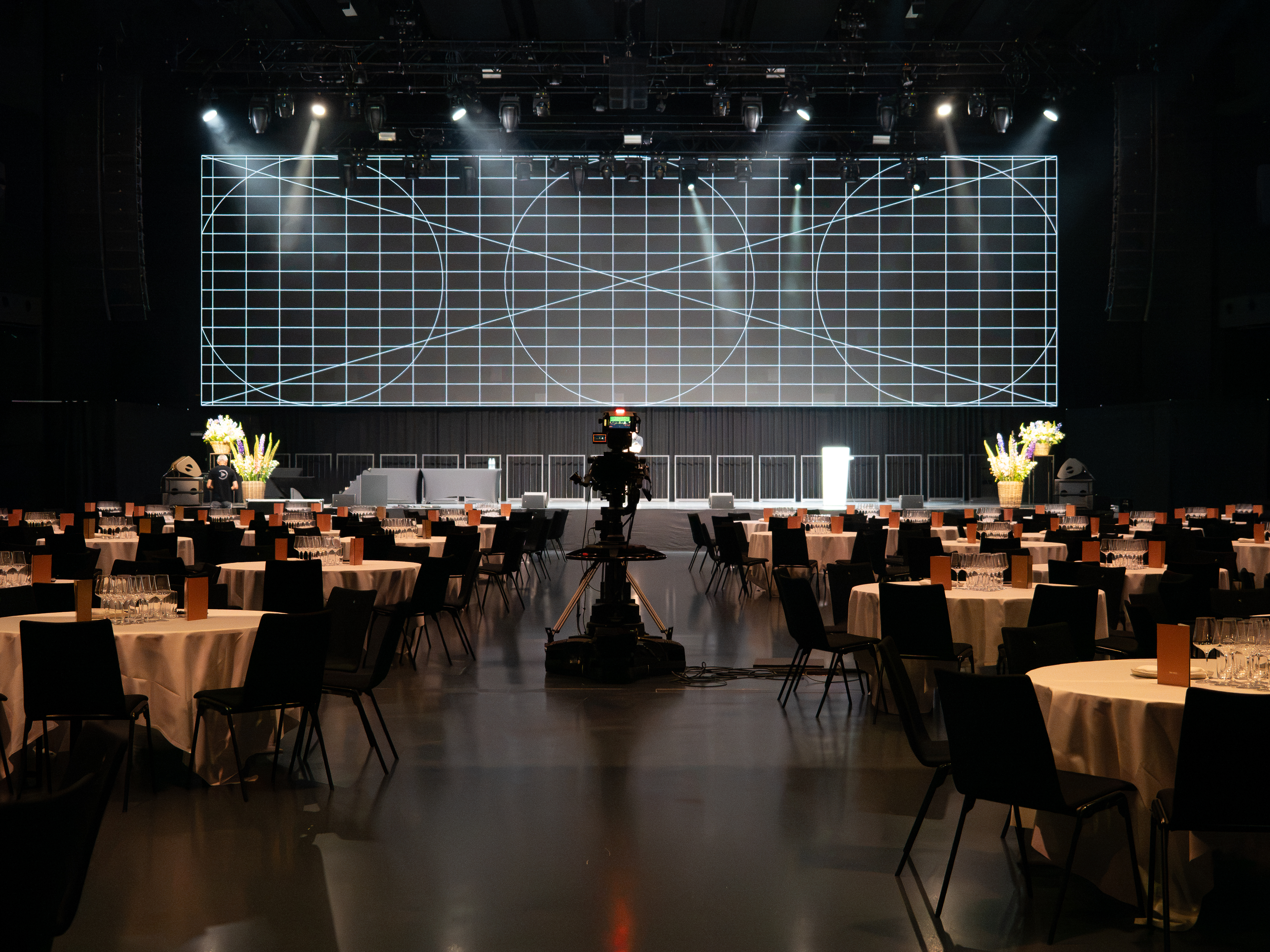 Gala-Setup in der HALL mit runden Tischen, Bühne, grosser LED-Wand und Videokamera.